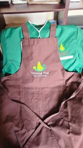 Branded work attire with embroidered chicken-and-cup logo and text “Chicking Plus – Taste, Brew & Play!”