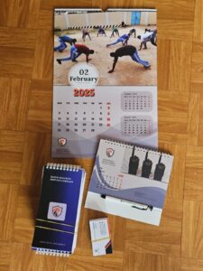 Wall calendar, desk calendar, notebook, pen, and business cards featuring eagle logo and slogan “Your Safety, Our Mission.”