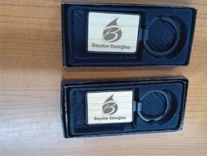 Rectangular wooden keychains engraved with Baystar Energies logo and flame design, presented in black gift boxes as promotional branded merchandise.