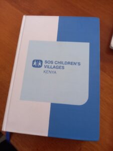 Blue and white notebook cover printed with SOS Children’s Villages Kenya logo, branded organizational stationery.