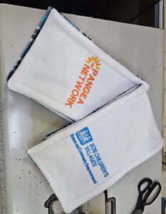 White fleece scarves embroidered with The Pangea Network logo and SOS Children’s Villages community empowerment text, promotional textile branding.